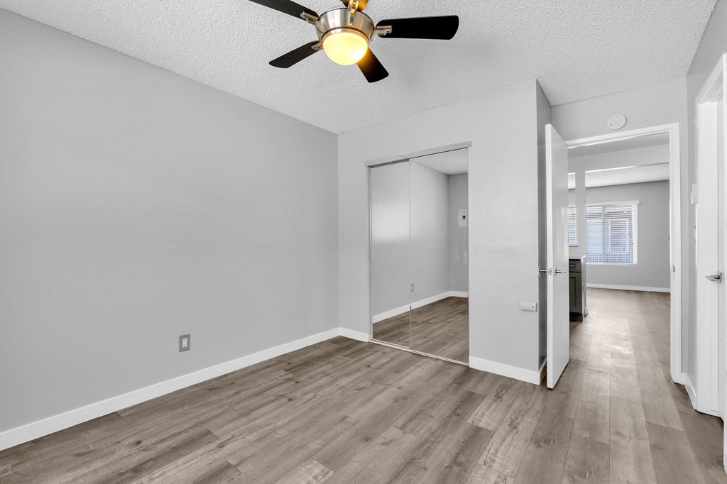 the living room and dining room of an apartment with white walls and a ceiling fan