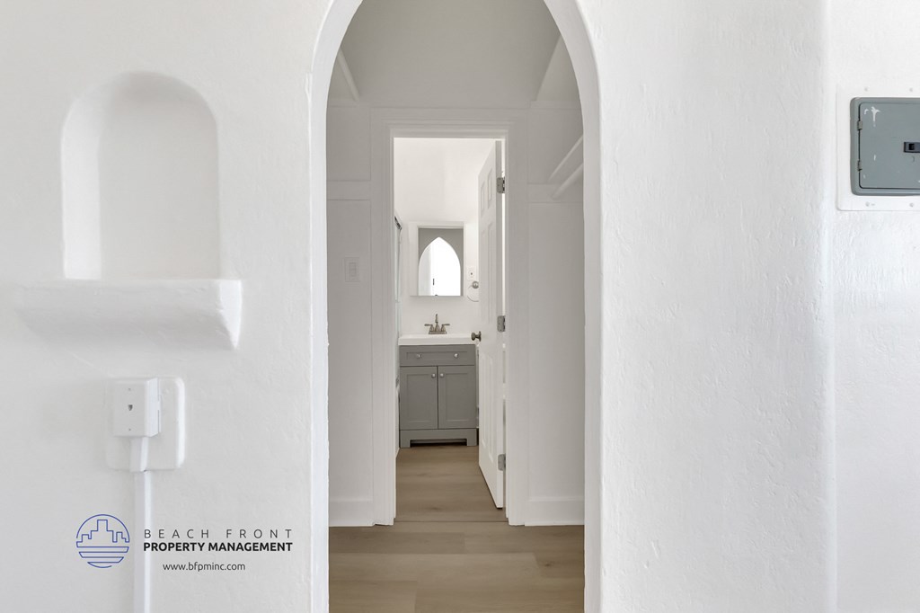 the hallway of a white house with a bathroom and a sink