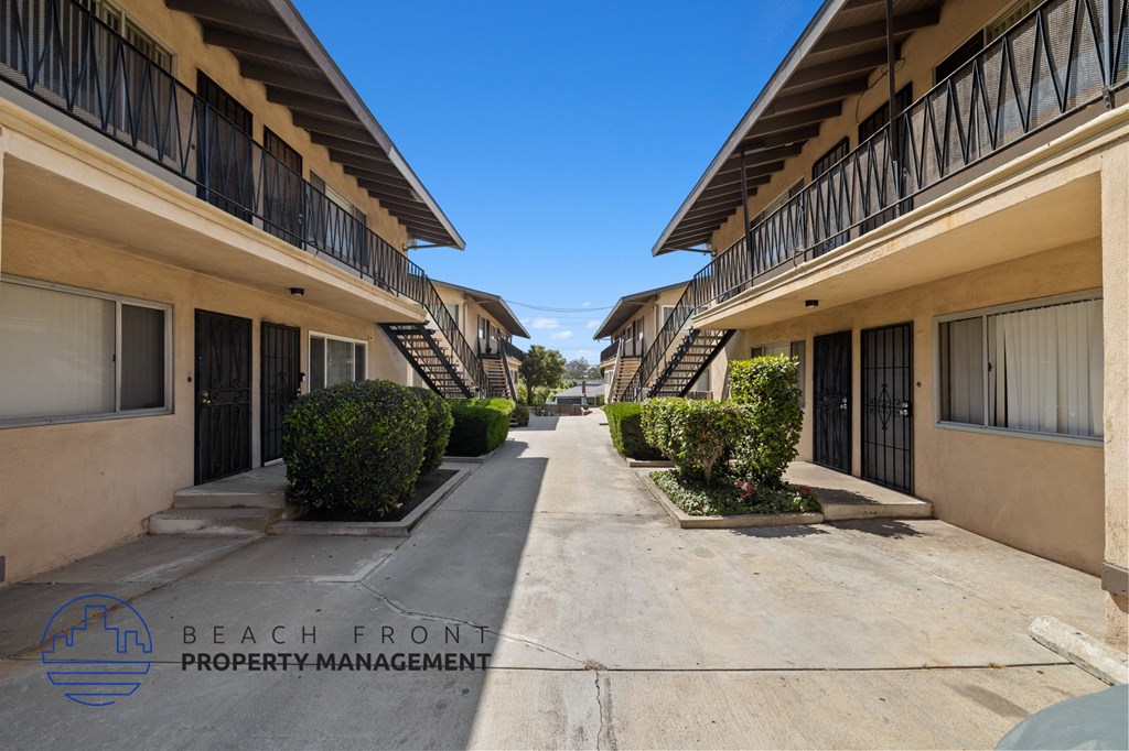 a long walkway between two buildings with balconies and bushes
