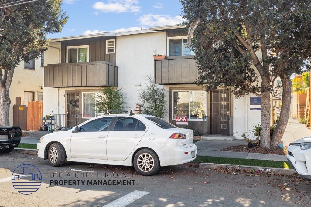A white car is parked in front of a two-story building with a sign that reads "BEACH FRONT PROPERTY MANAGEMENT.".