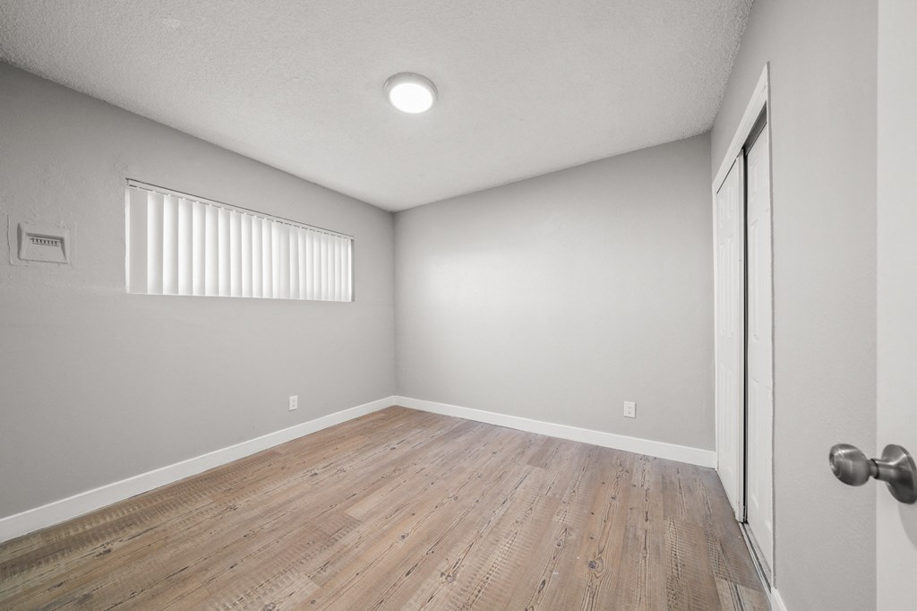 the spacious living room with wood flooring and a door to the bedroom
