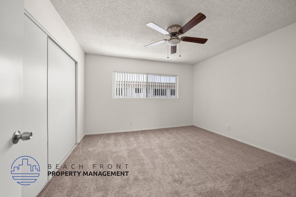 A room with a carpeted floor, a ceiling fan, and a window with blinds.
