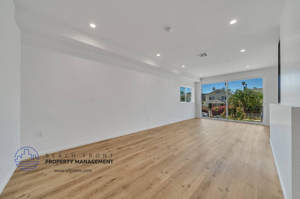 a living room with white walls and wood flooring and a balcony