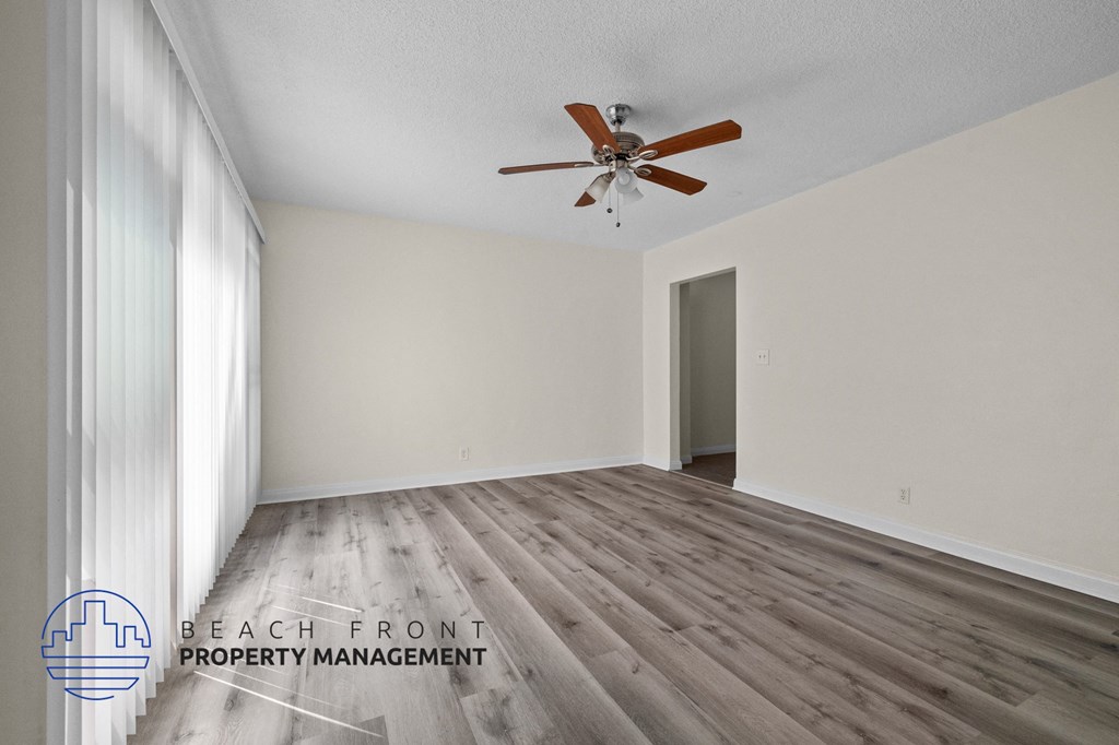 the spacious living room with hardwood flooring and a ceiling fan
