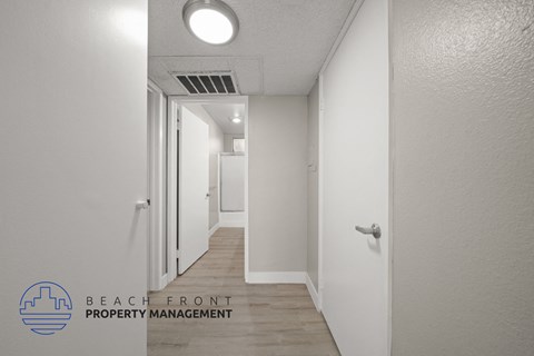 a renovated hallway with white walls and wood flooring and a door to a closet