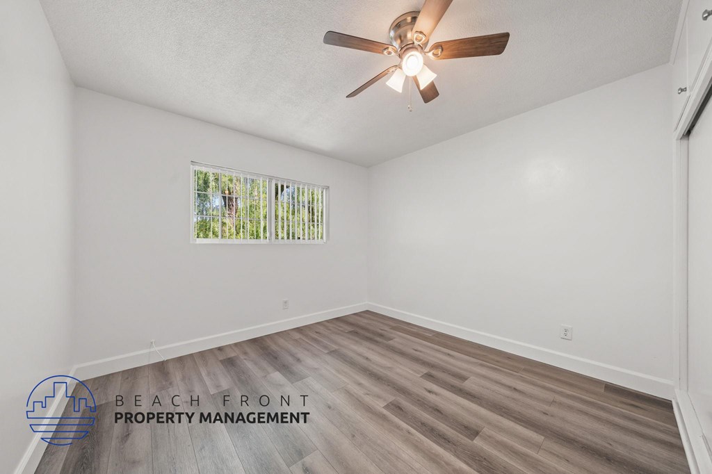 A room with a ceiling fan and a window showing greenery outside.