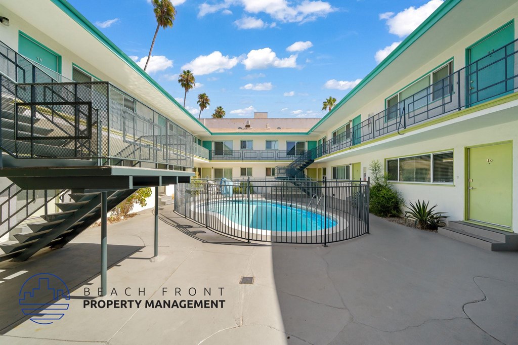A pool is surrounded by a fence and a building with a balcony.