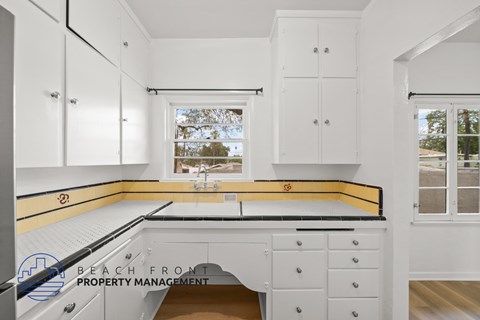 A kitchen with white cabinets and a window overlooking a beach.