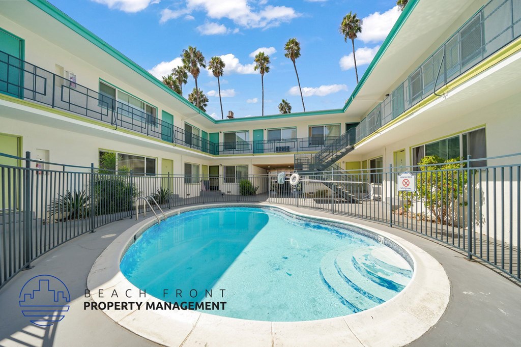 A pool in a courtyard surrounded by buildings with a sign that says "Beach Front Property Management".