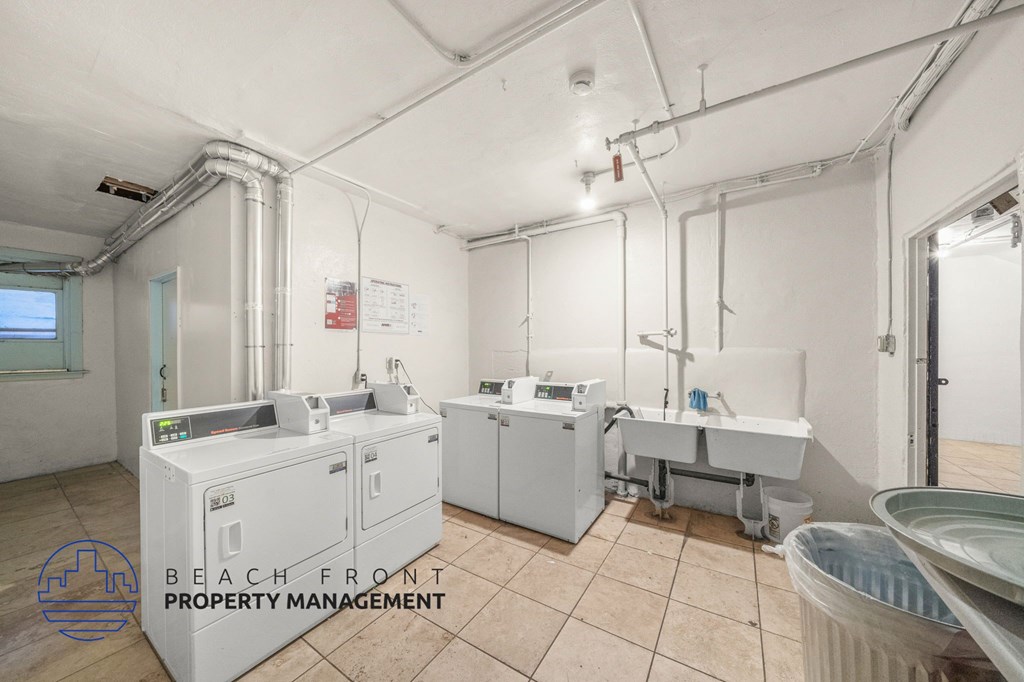 A clean, empty room with a washing machine and a dryer, with the logo of Beach Front Property Management in the corner.