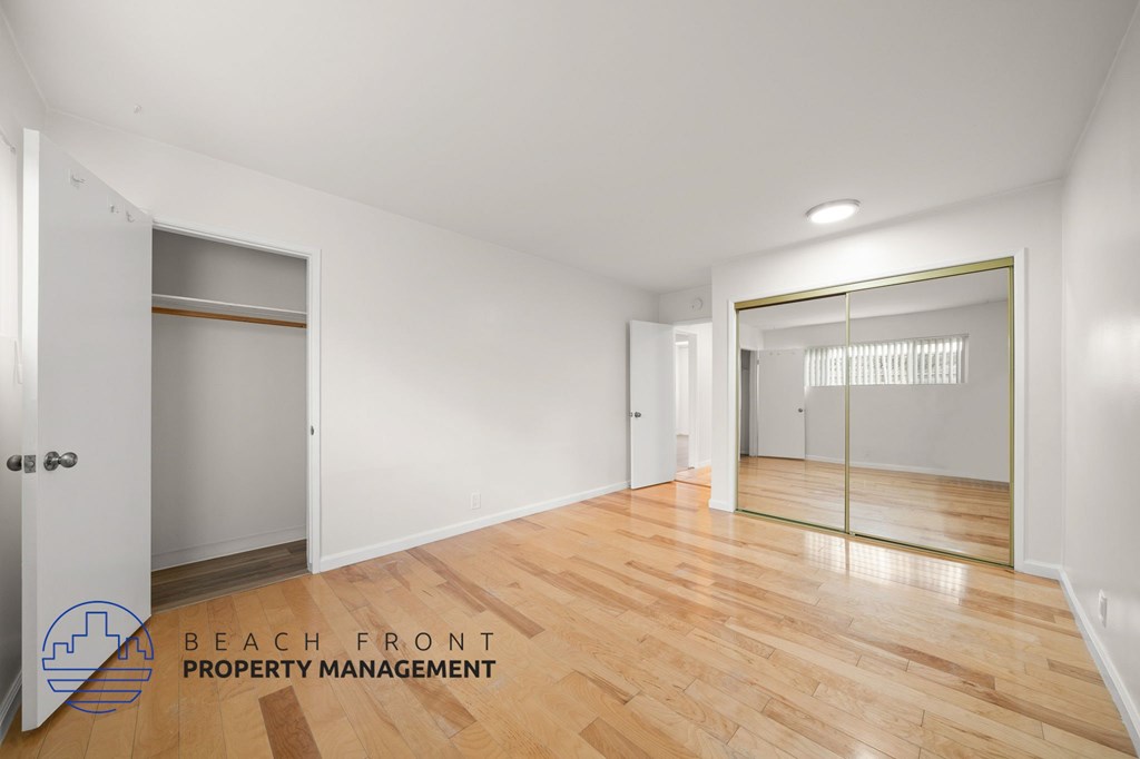 A room with wooden floors and white walls, with a glass door leading to another room.
