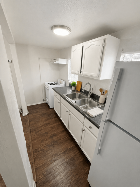 A kitchen with white appliances and wooden floors.