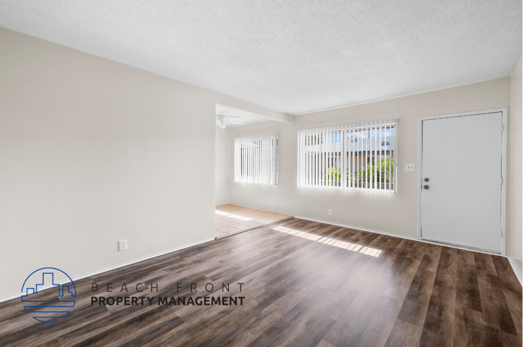 the living room and dining room of an apartment with wood flooring and a door