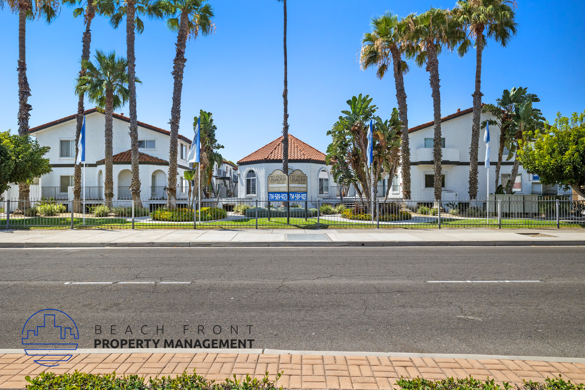 A street view of a beachfront property with palm trees and a building with a red roof.