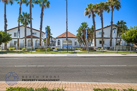 A street view of a beachfront property with palm trees and a building with a red roof.
