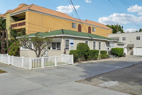 A white picket fence in front of a yellow building.