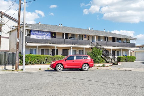 A red car is parked in front of a two-story building.