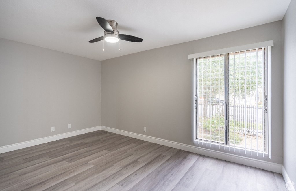 an empty living room with a large window and a ceiling fan