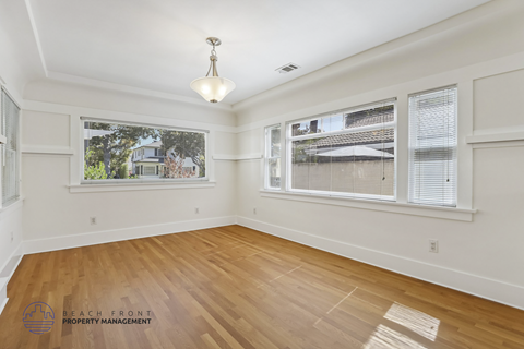 A room with wooden floors and white walls, with a window showing a view of a house.