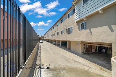 A view of a street with buildings on both sides and a fence on the left.