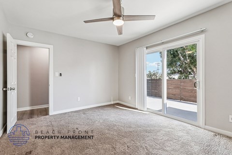 A spacious room with a ceiling fan and sliding glass doors leading to a backyard.