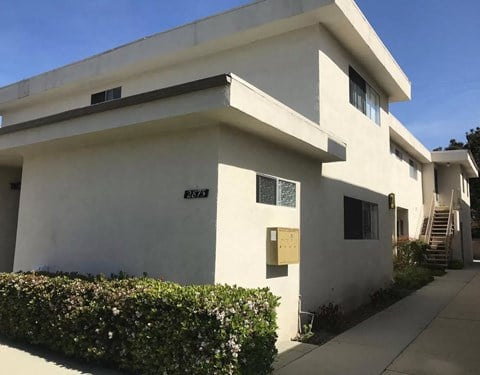 a white building with a sidewalk and bushes in front of it