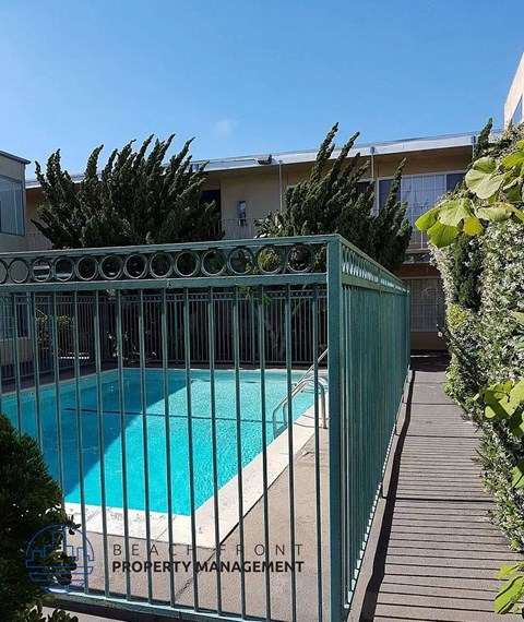 A pool surrounded by a green fence with the words "Beachfront Property Management" written on it.