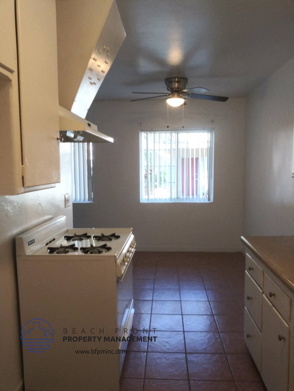 an empty kitchen with a stove and a ceiling fan