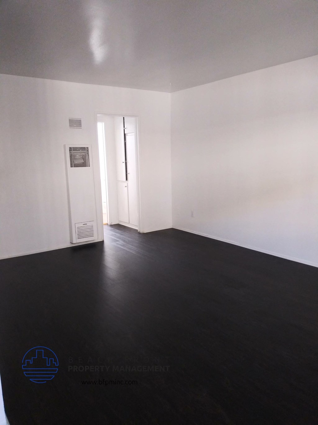an empty living room with white walls and a dark wood floor