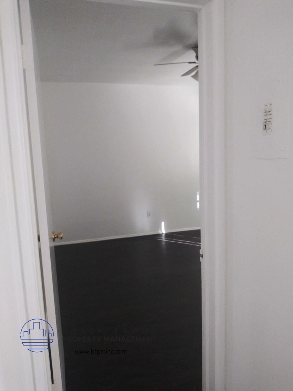 a room with white walls and a black floor and a ceiling fan