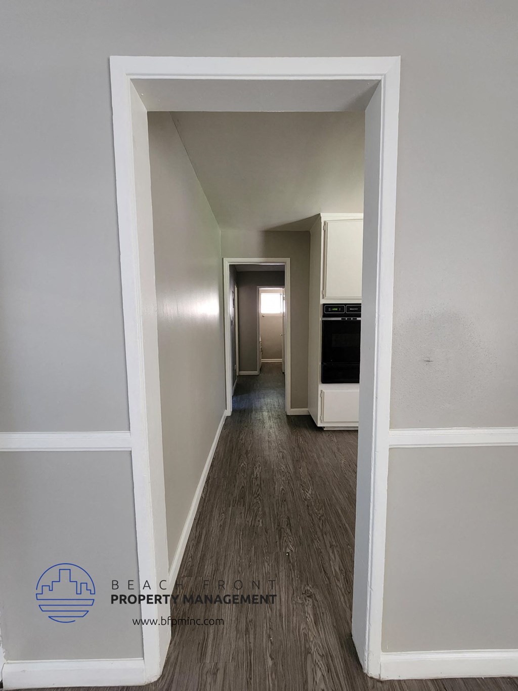 an empty hallway with a hallway door open to a kitchen and a living room