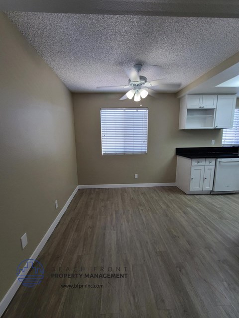 an empty living room with a kitchen and a ceiling fan