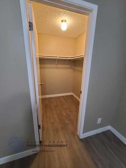 a walk in closet in an empty room with wooden floors