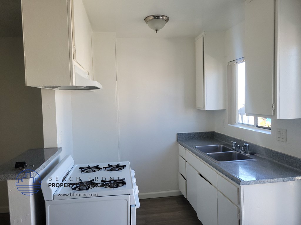 an empty kitchen with white cabinets and a stove and sink