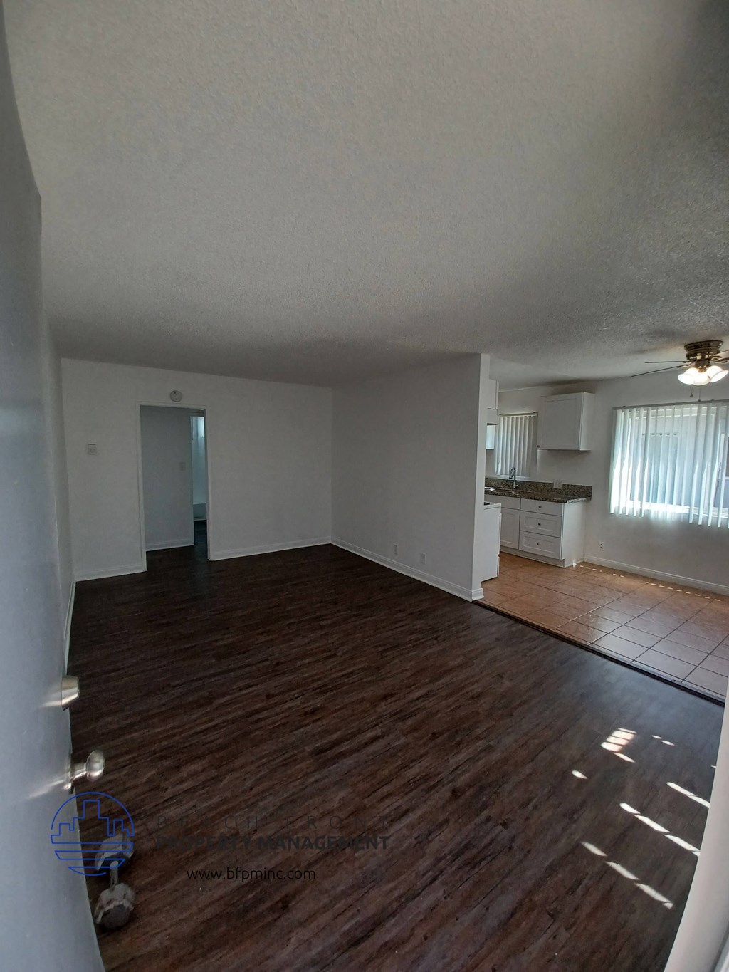 an empty living room with hardwood floors and a kitchen in the background