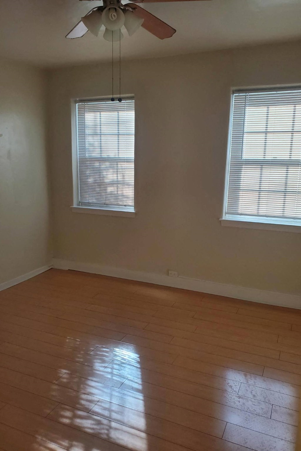 an empty living room with a ceiling fan and two windows