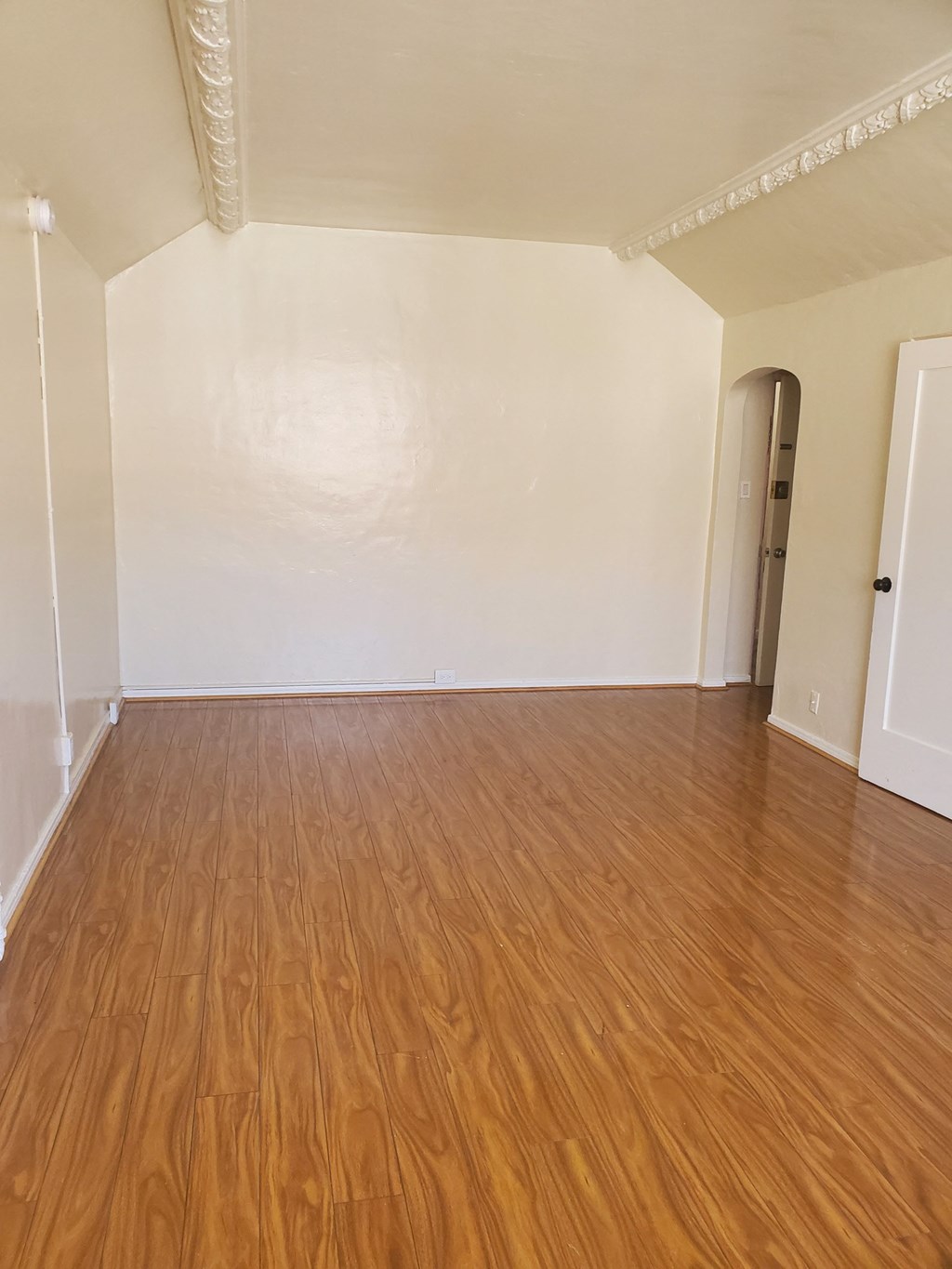 an empty living room with wood flooring and a white wall