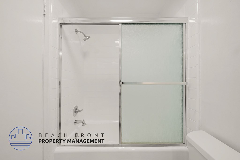 A shower area with a glass door and a white bathtub.