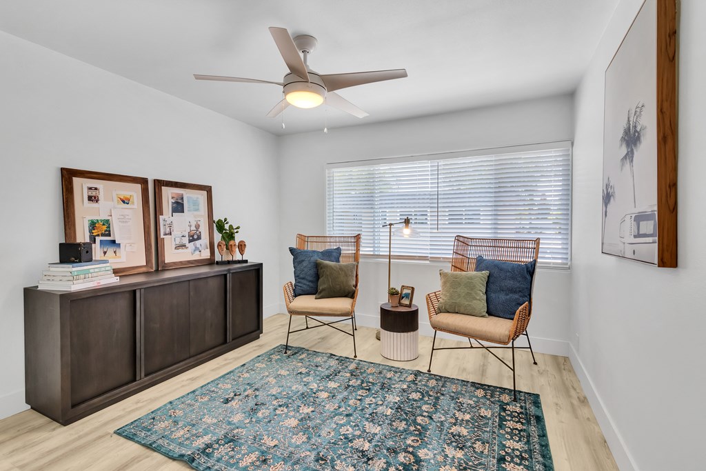 A room with a rug, two chairs, a table, and a fan.