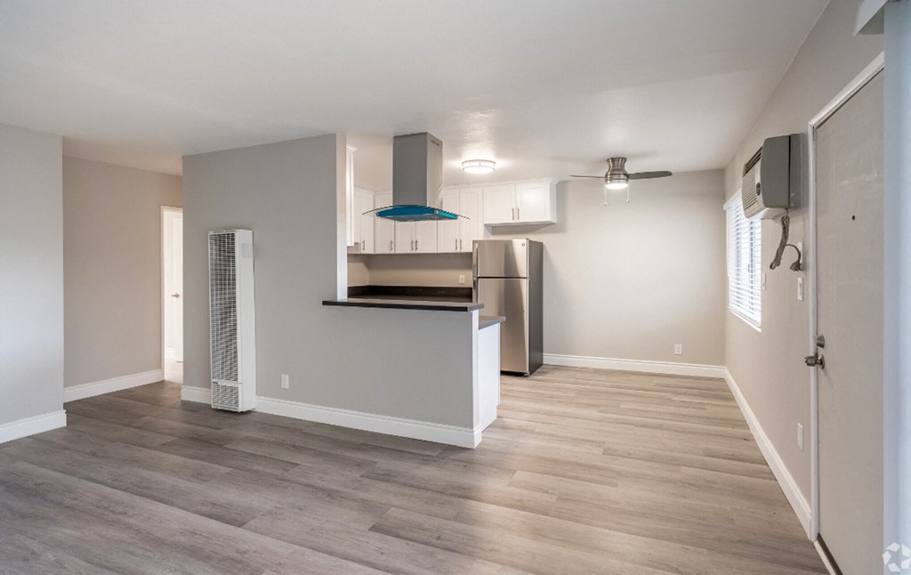 an empty living room and kitchen with a refrigerator and a microwave