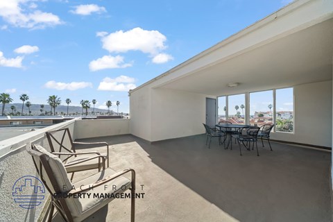A balcony with chairs and a table is overlooking a pool and palm trees.