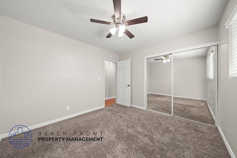 A spacious room with a ceiling fan and a sliding glass door leading to a balcony.