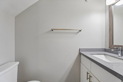 A white toilet sits in a small bathroom with a sink and mirror.