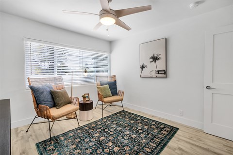 A room with a rug, two chairs and a ceiling fan.