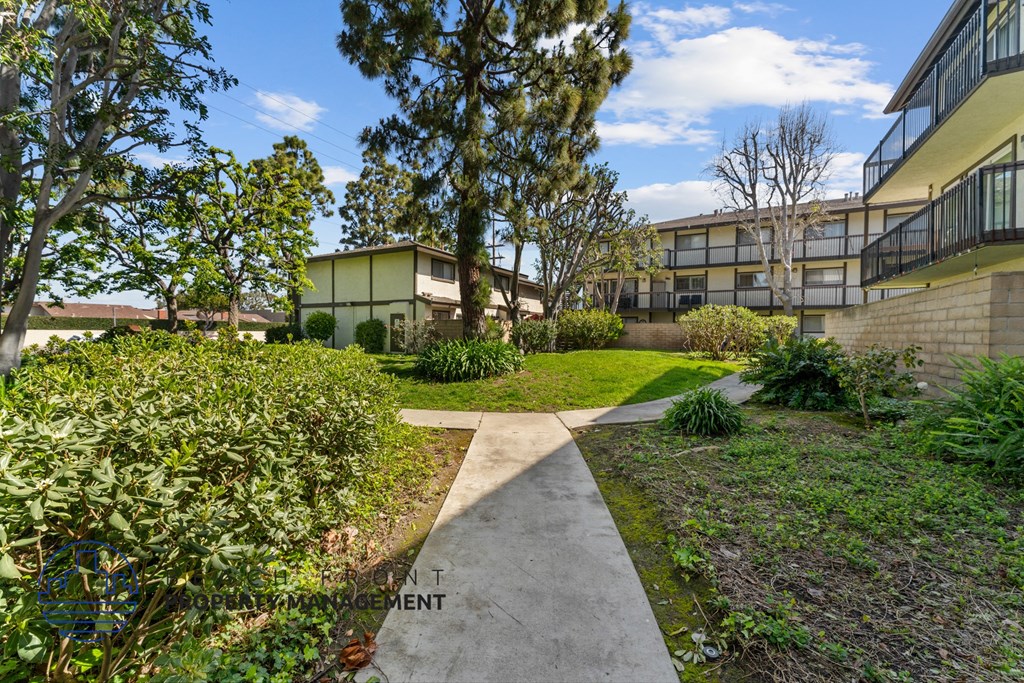 A concrete walkway leads through a landscaped area with a building in the background.