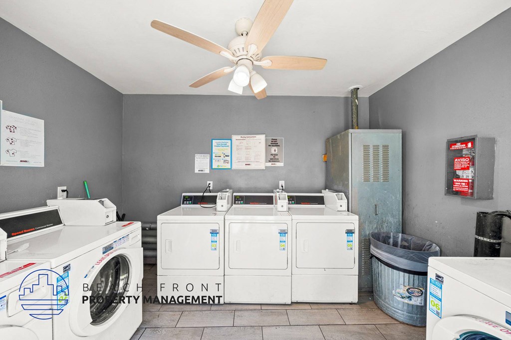 A laundry room with a washer and dryer, a fan, and a trash can.