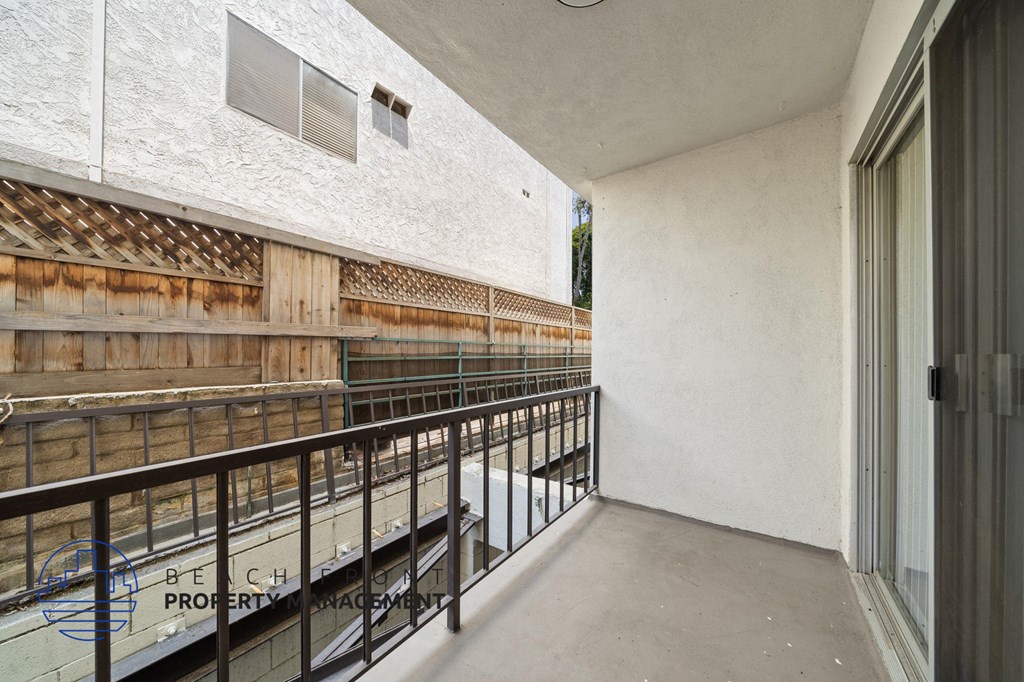 A balcony with a metal railing and a white wall with a window.