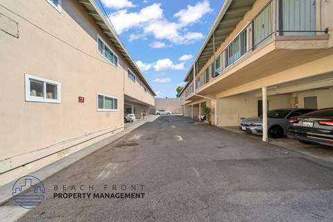 A parking lot between two buildings with the logo of Beach Front Property Management in the bottom left corner.