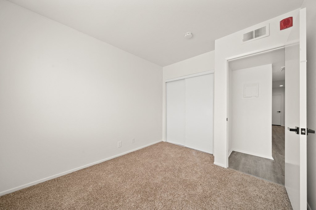 a bedroom with white walls and carpet and a door to a closet