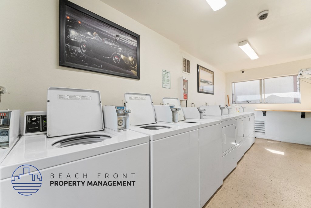 A laundry room with washers and dryers, a framed picture of a car on the wall, and a sign that says "Beach Front Property Management".